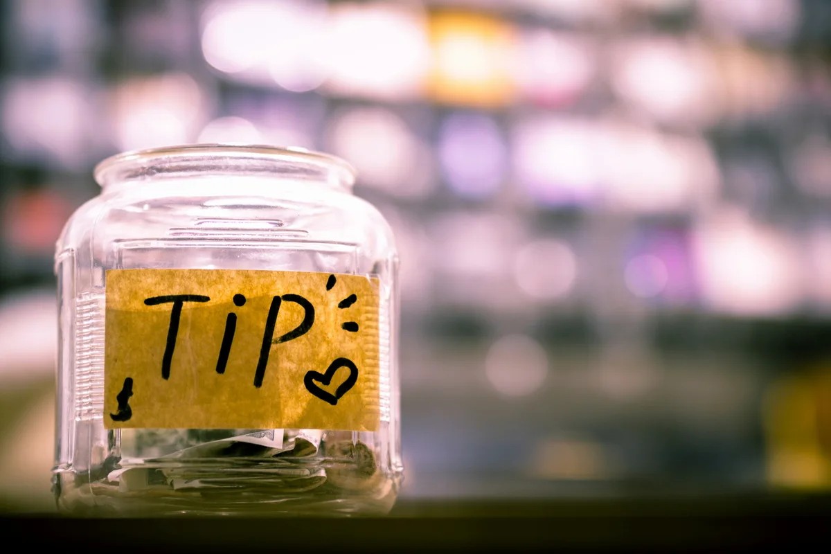 Glass tip jar with coins on a counter, representing tipping culture and calculators